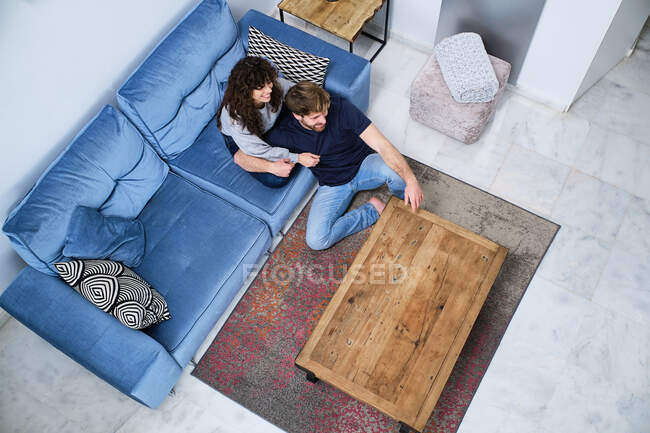 Vista superior de la feliz pareja joven con ropa casual sentada en el sofá y abrazando mientras pasan tiempo juntos - foto de stock