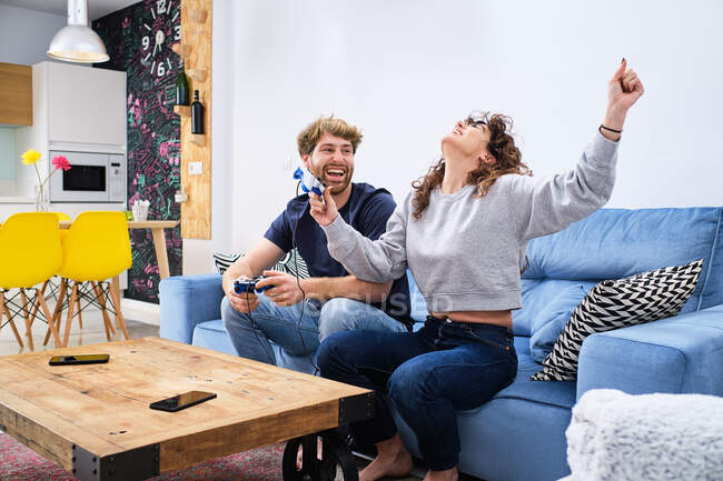 Vista lateral de alegre e animado jovem casal em roupas casuais jogando videogame no console na elegante sala de estar — Fotografia de Stock