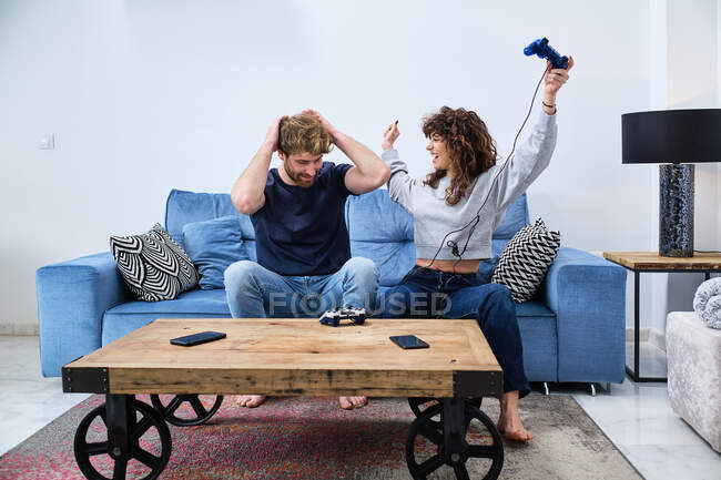 Весела і збуджена молода пара в повсякденному одязі грає в відеоігри на консолі в стильній вітальні — стокове фото