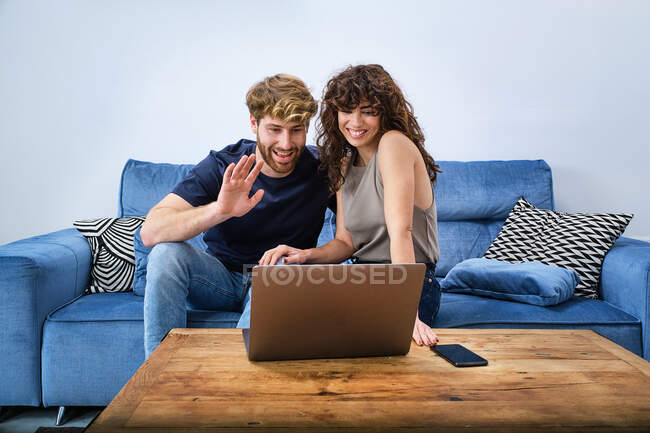 Junges glückliches Paar in lässiger Kleidung unterhält sich online auf Laptop auf Sofa im Wohnzimmer — Stockfoto