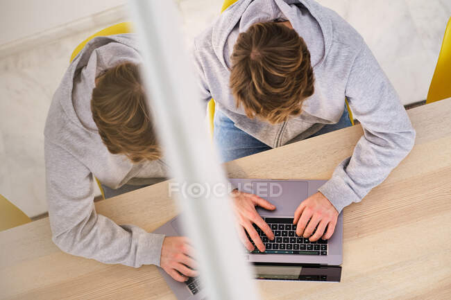 Von oben ein anonymer Mann in lässiger Kleidung, der auf einem Stuhl neben einem Tisch sitzt und Netbook in einer hellen Wohnung benutzt — Stockfoto