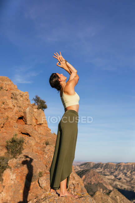 Vista laterale di sottile femmina in abito casual esecuzione di montagna con le braccia in alto e postura Backbend sul pendio della montagna rocciosa — Foto stock