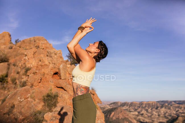 Vista laterale di sottile femmina in abito casual esecuzione di montagna con le braccia in alto e postura Backbend sul pendio della montagna rocciosa — Foto stock