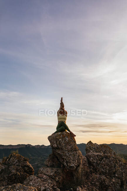 Низкий угол покоя женщины в коровьем лице позируют с руками орла выполняя упражнения йоги на скалистой земле на ярком закате — стоковое фото