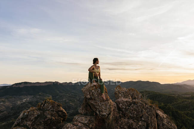 Giovane donna fiduciosa a piedi nudi in activewear rilassante sulla scogliera rocciosa mentre ha pratica yoga all'alba — Foto stock