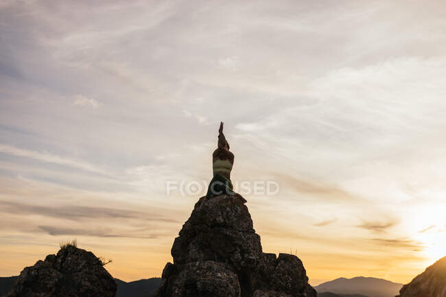 Low angle of calm female in cow face pose with eagle pose arms performing yoga exercise on rocky ground at bright sunset — Stock Photo