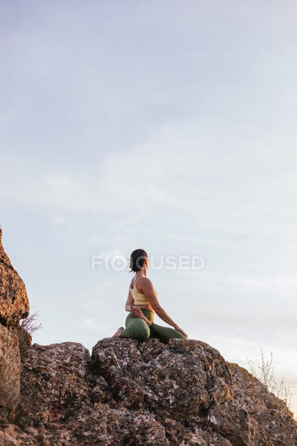 Низький кут спокійної невпізнаваної жінки, що виконує вправи з йоги, практикуючи медитацію на кам'янистій землі на яскравому заході сонця — стокове фото
