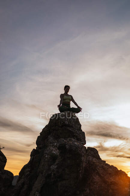 Low angle of calm female performing yoga exercise while practicing on rocky ground at bright sunset — Stock Photo