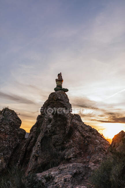 Basso angolo di calma femminile seduta in posa di loto con mani di preghiera che eseguono esercizio di yoga praticando su un terreno roccioso al tramonto luminoso — Foto stock