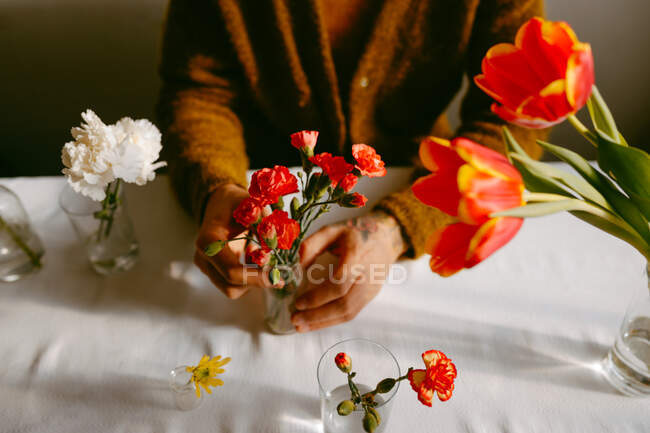 Високий кут врожаю анонімний чоловічий флорист, що сидить за столом з гвоздиками і тюльпанами в скляному посуді — стокове фото