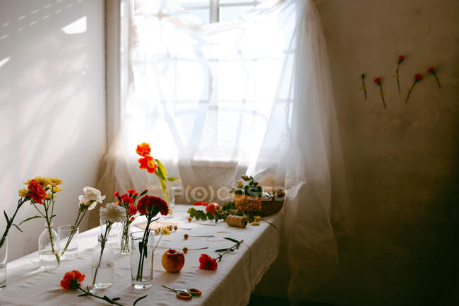 Vasos de tulipanes frescos y claveles en agua colocados sobre la mesa para hacer ramos - foto de stock