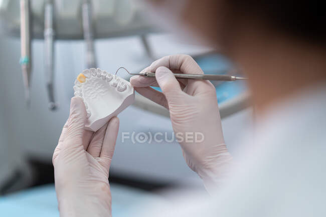 Crop unrecognizable orthodontist with surgical tools making cast of jaw for patient while working in modern clinic — Stock Photo