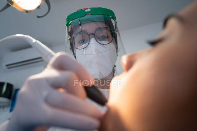 Professional dentist in uniform with medical mask drilling tooth of calm woman with help of assistant — Fotografia de Stock