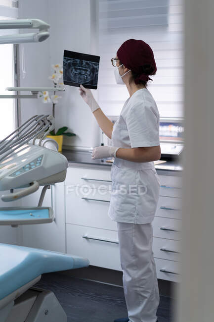 Seitenansicht eines wehmütigen Arztes in Uniform, der das Röntgenbild des Patienten untersucht, während er über die Diagnose nachdenkt — Stockfoto