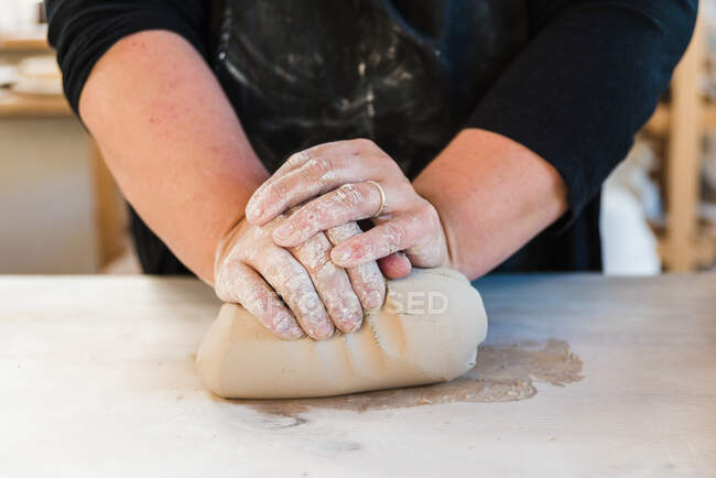 Crop unrecognizable female master in black casual outfit rolling clay on table in light studio before making clay object — Stock Photo