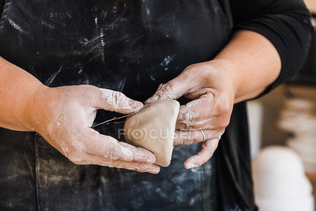 Обрізати анонімного майстра в брудному фартусі, стоячи в майстерні і формуючи шматок глини, позначивши його квіткою в руках — стокове фото