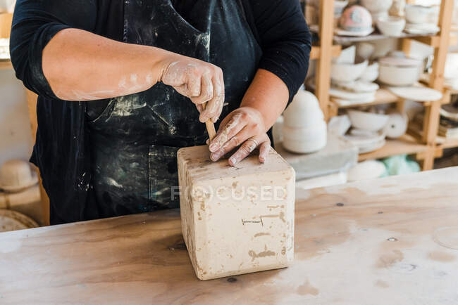 Анонимная женщина-мастер в фартуке убирает глиняный горшок из плесени на столе в мастерской керамики — стоковое фото