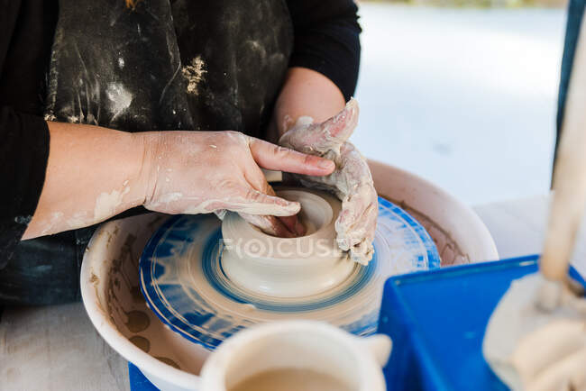 Crop anonymous female artisan in apron modeling clay pot on throwing wheel — Foto stock