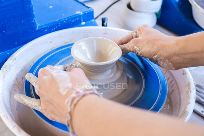 From above crop anonymous female artisan in apron modeling clay pot on throwing wheel — Stock Photo