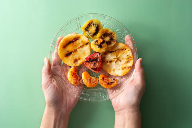 Mains de femme tenant assiette de fruits grillés sur fond vert — Photo de stock
