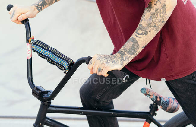 Side view of crop anonymous hipster male biker riding BMX bicycle in skate park in daytime — Stock Photo