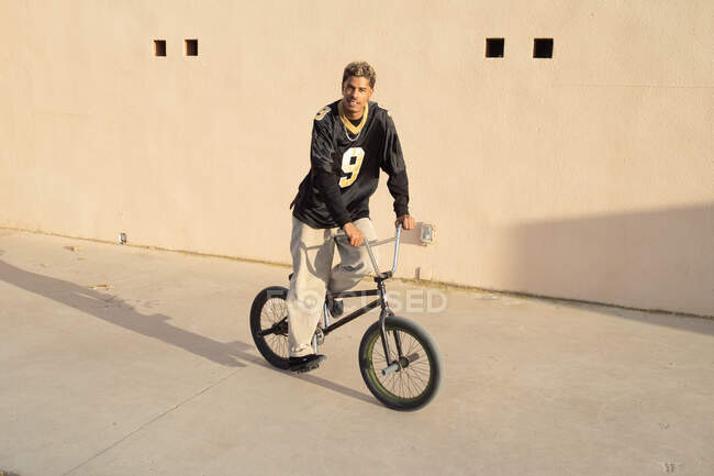 Vista lateral do jovem esportista afro-americano realizando truque em bicicleta de julgamento no parque de skate na cidade — Fotografia de Stock