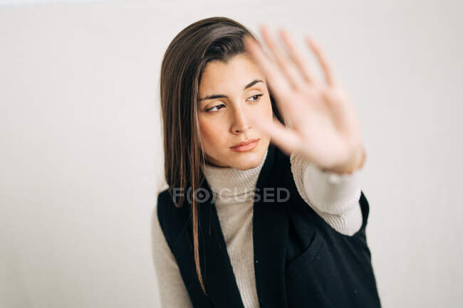 Молодая созерцательная женщина в повседневной одежде демонстрирует отрицание жеста с протянутой рукой, глядя в сторону в дневное время — стоковое фото