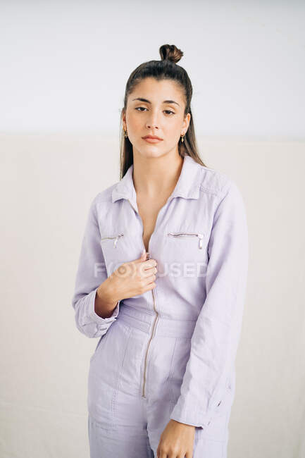 Unemotional young thoughtful female in stylish overall looking at camera standing in studio background — Stock Photo