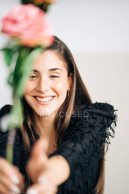 Молода щаслива жінка в чорному одязі з квітучою квіткою дивиться на камеру з зубною посмішкою — стокове фото