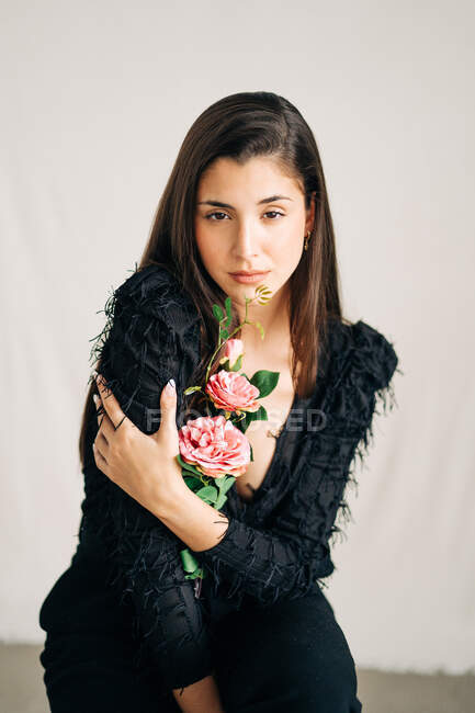 Молода чуттєва жінка в чорному одязі з квітковою квіткою, що дивиться на камеру. — стокове фото