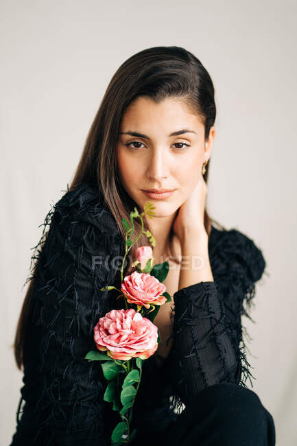 Молодая чувственная женщина в черной одежде с цветущим цветком, смотрящая в камеру — стоковое фото