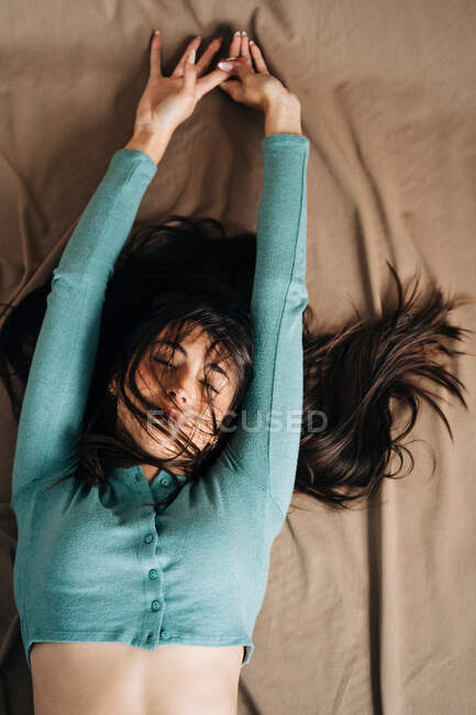 Top view of young mindful female with closed eyes lying on bed with crumpled textile at home — Stock Photo