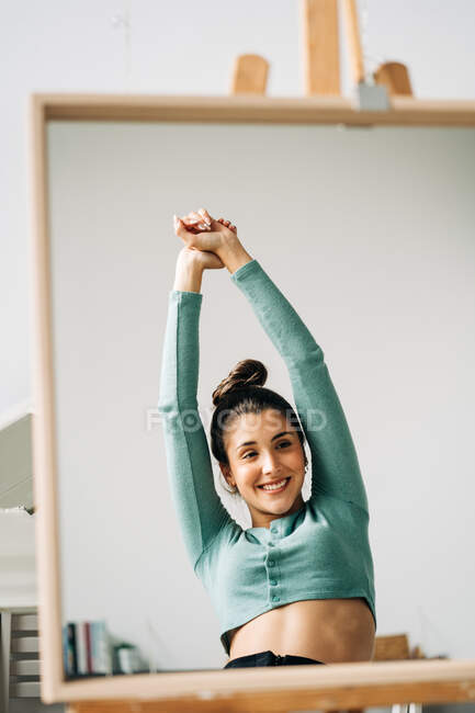 Cheerful female with raised arms and hair bun reflecting in mirror in house in daytime — Stock Photo