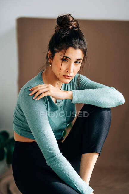 Young wistful female in casual clothes sitting against brown fabric background looking at camera — Stock Photo