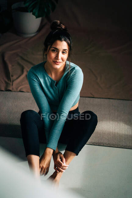 Young wistful female in casual clothes sitting on floor against potted plant on crumpled fabric and looking away — Stock Photo