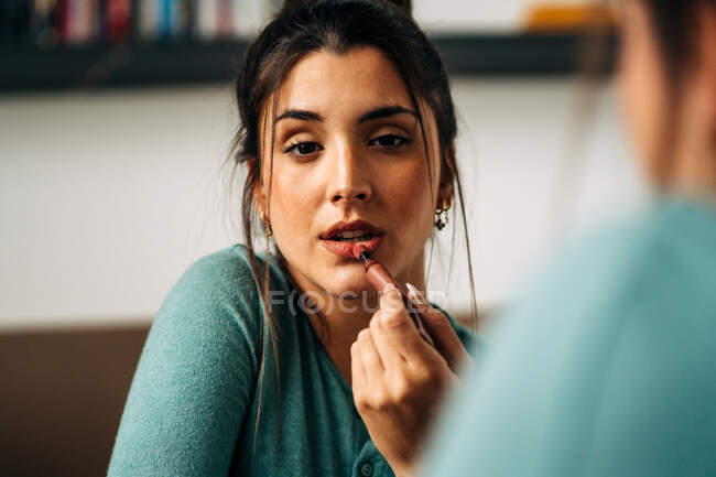 Erntehelferin trägt Lippenstift auf den Lippen auf, während sie zu Hause bei Tageslicht in den Spiegel schaut — Stockfoto