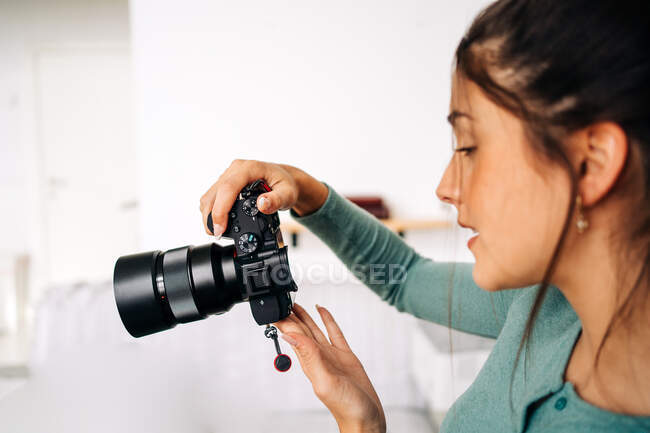 Millennial female with professional photo camera sitting light background at home — Stock Photo