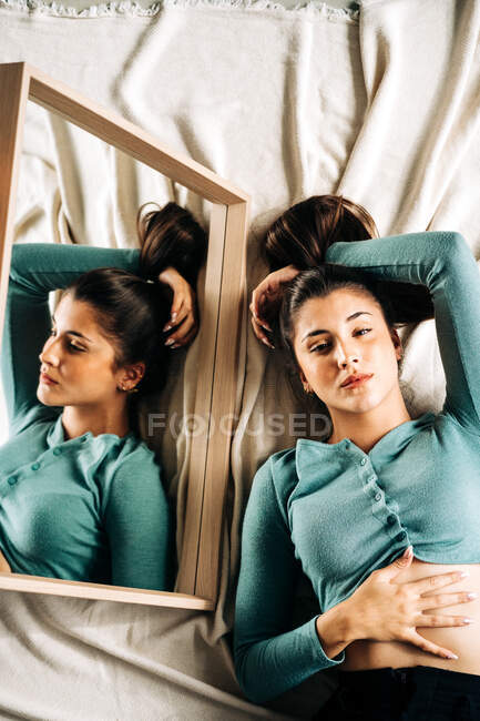 Top view of millennial female with hand behind head looking at camera against mirror on crumpled fabric — Stock Photo