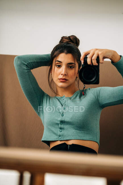 Jovem mulher em roupa casual com câmera fotográfica digital profissional refletindo no espelho em casa — Fotografia de Stock