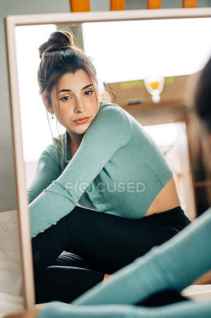 Jovem mulher pensativa sentada no chão olhando para a câmera no espelho — Fotografia de Stock