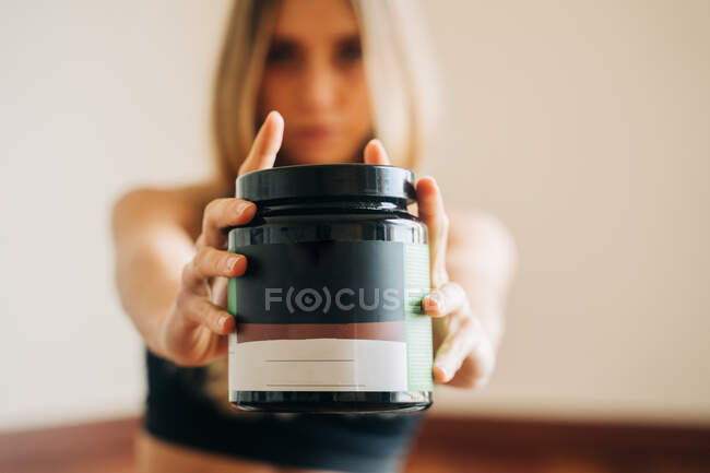 Blurred anonymous female wearing activewear with sports nutrition jar for body building in hands standing in room during training at home — Stock Photo