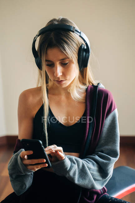 Fit female in headphones listening to music and surfing cellphone after workout at home — Stock Photo