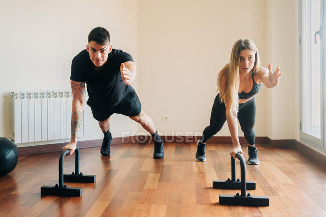 Determined man and woman practicing exercise using steel push ups stands while building chest muscles during workout in room at home — Stock Photo