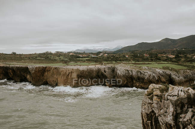 Живописный пейзаж скалистой скалы рядом с волнистым морем под облачным небом в пасмурный день — стоковое фото