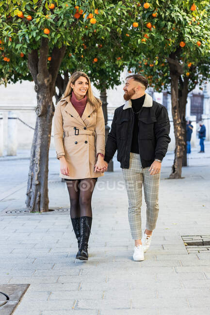 Casal apaixonado vestindo roupas da moda de mãos dadas e andando ao longo da rua enquanto desfruta do dia de folga na cidade — Fotografia de Stock