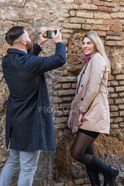 Парень с фотокамерой фотографирует очаровательную девушку, стоящую на городской улице во время прогулки по городу в выходные дни — стоковое фото