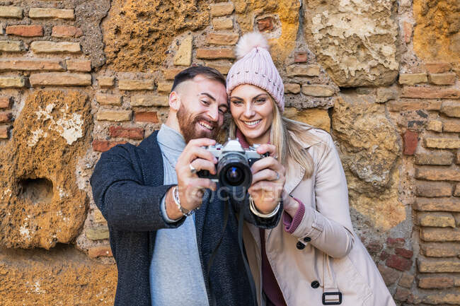 Boyfriend with photo camera showing picture to charming girlfriend standing in urban street during weekend stroll in town — Stock Photo