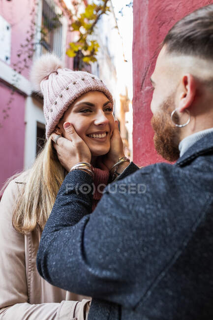 Vue latérale de la culture tendre homme méconnaissable embrassant femme charmante souriante tout en se tenant ensemble dans la ville pendant la promenade — Photo de stock