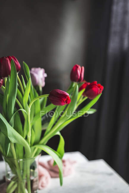 Jarrón de cristal con tulipanes rojos en la mesa junto a la ventana - foto de stock