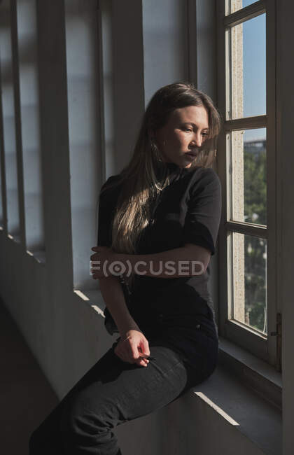 Retrato de menina bonita com cabelo loiro longo, ela está perto da janela e a luz do sol está iluminando seu rosto. — Fotografia de Stock